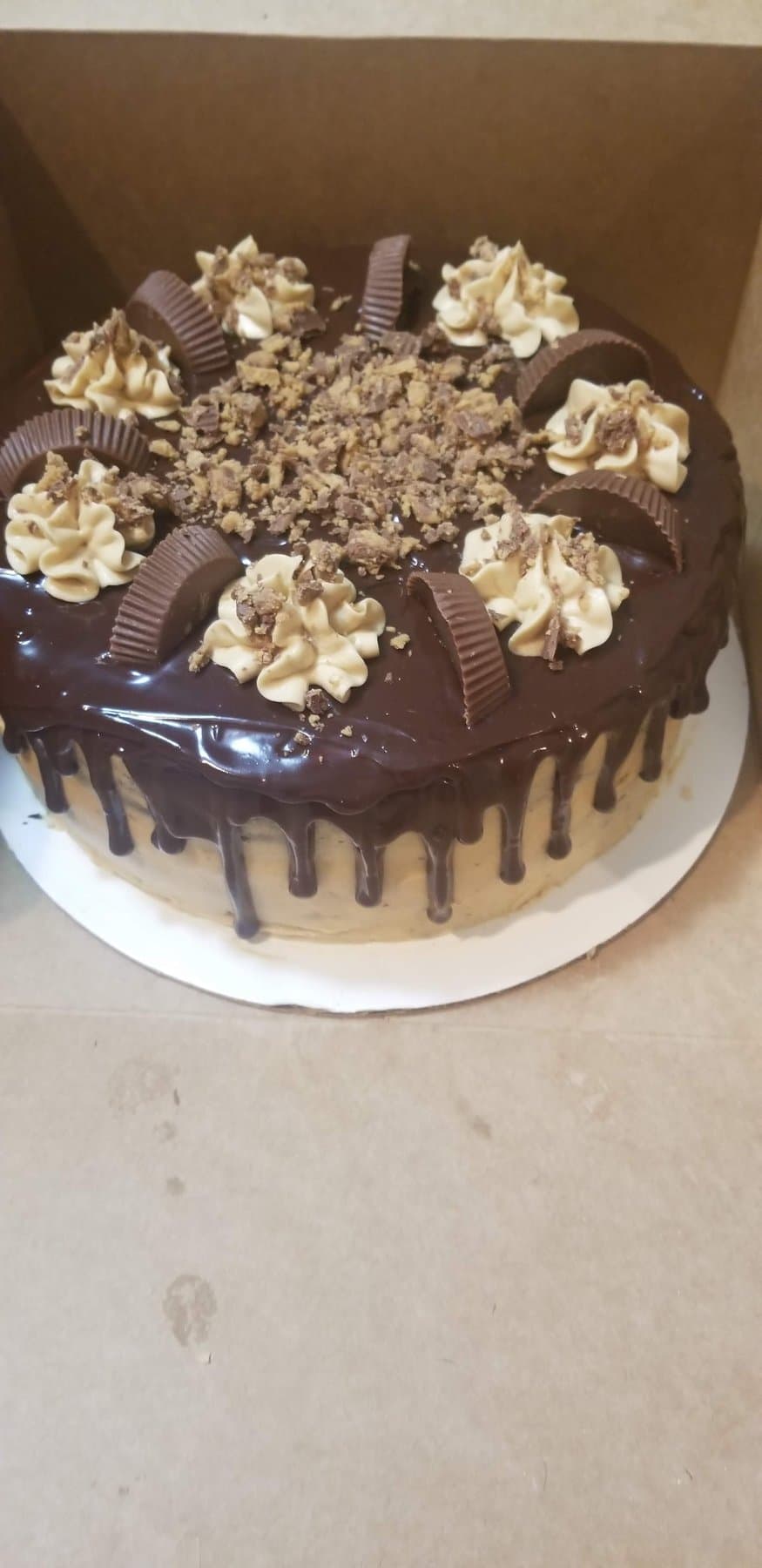 Chocolate drip cake topped with cookie crumbles and piped cream frosting by Jamie Cakes.