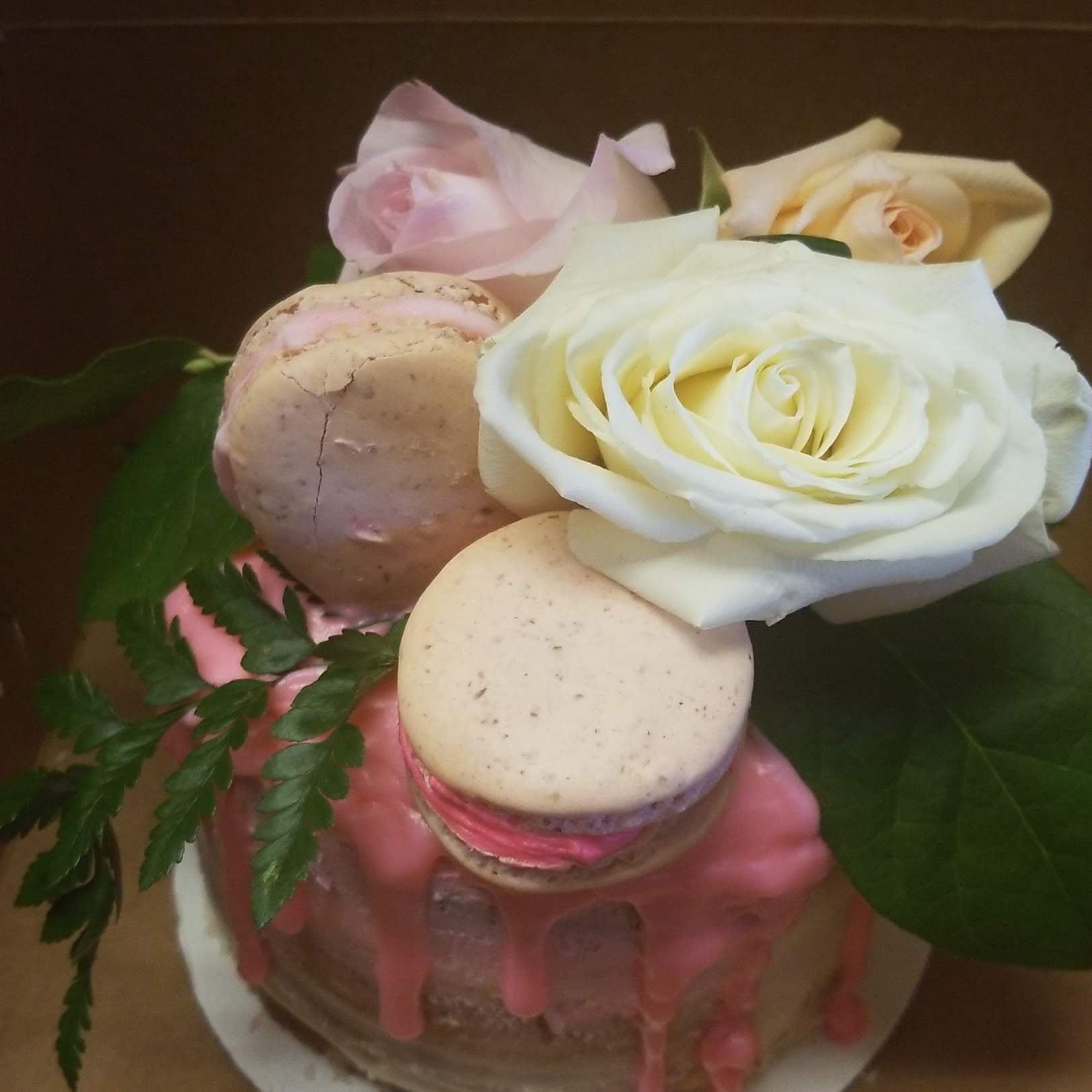 Close-up of a pink drip cake with roses and macarons by Jamie Cakes.